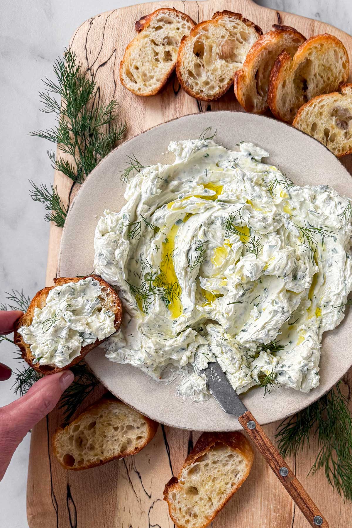 A spalted maple serving board with a bowl of Garlic Herb Cheese Dip, surrounded by crostini.