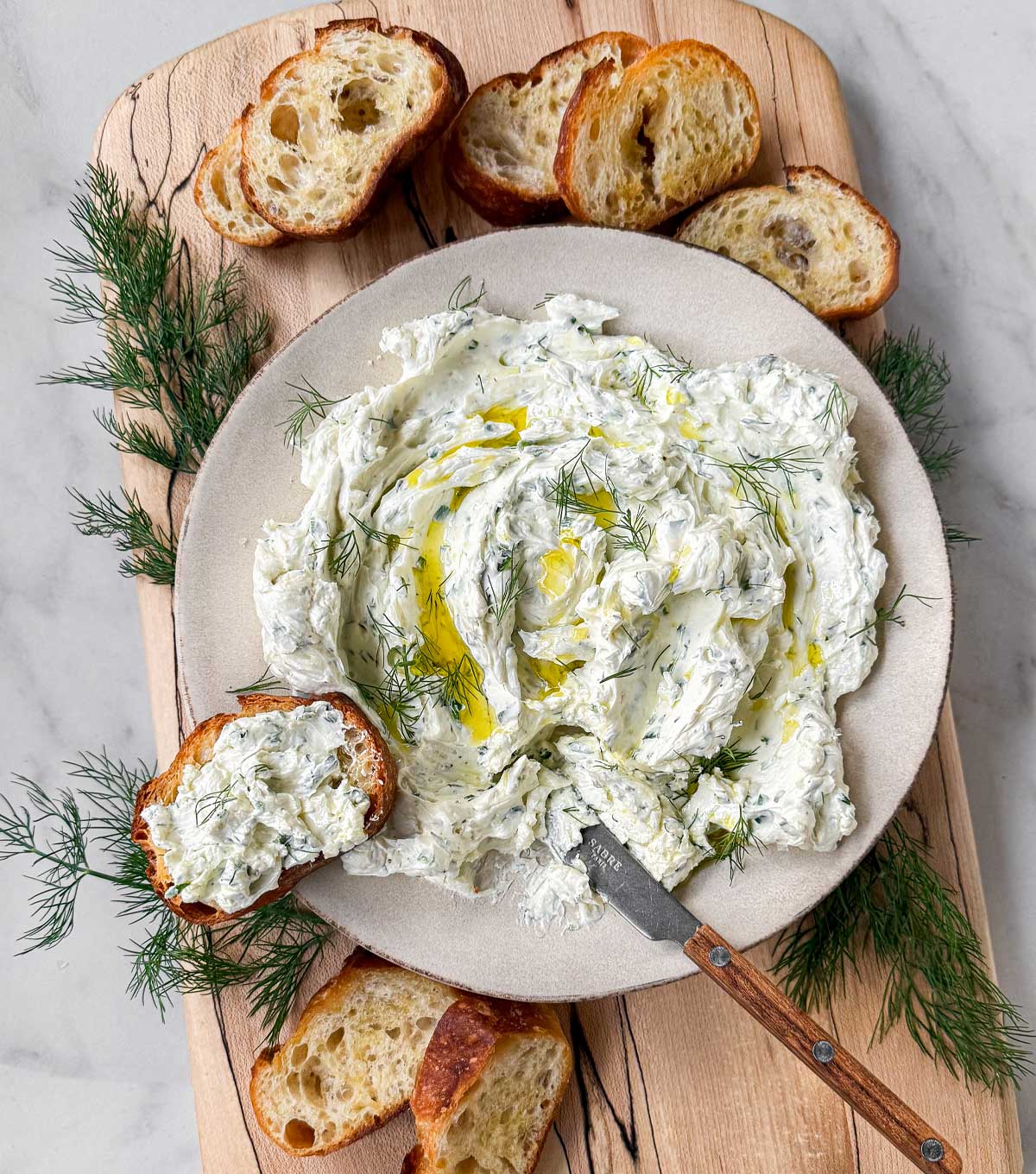 A bowl of garlic herb dip on a spalted maple serving board with crostini for dipping.