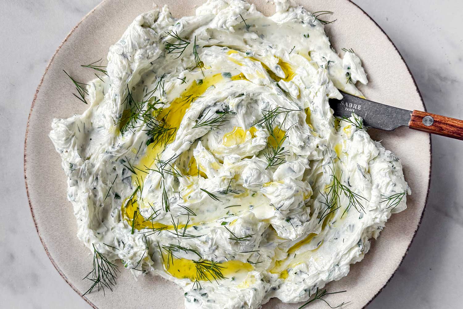 A bowl of Garlic Herb Cheese Dip, drizzled with olive oil and finished with flaky sea salt.