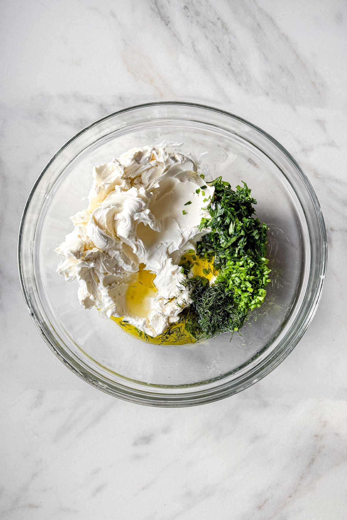 The ingredients for Garlic Herb Cheese Dip in a glass bowl