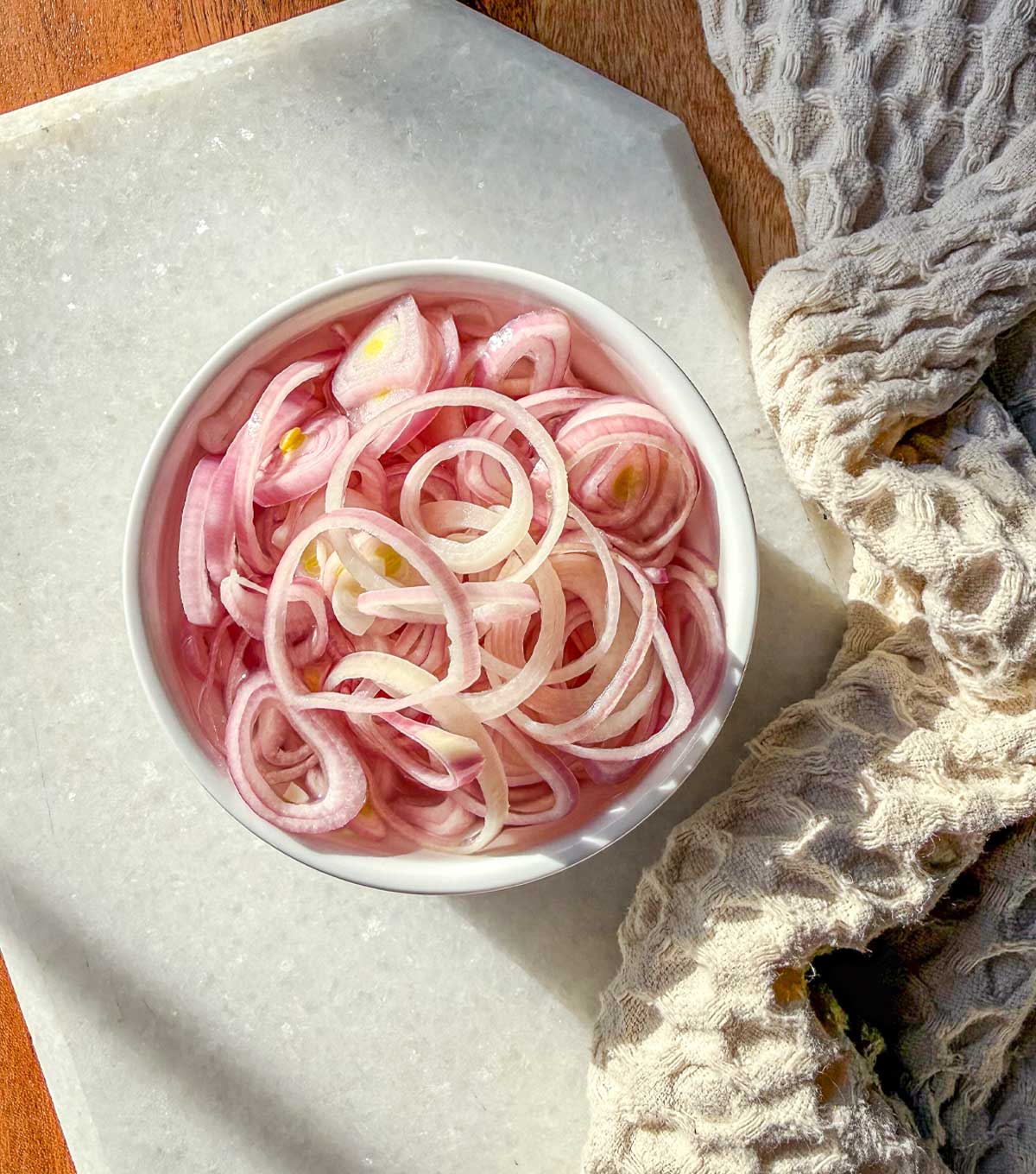Quick pickled shallots in a ramekin sitting on a marble board.