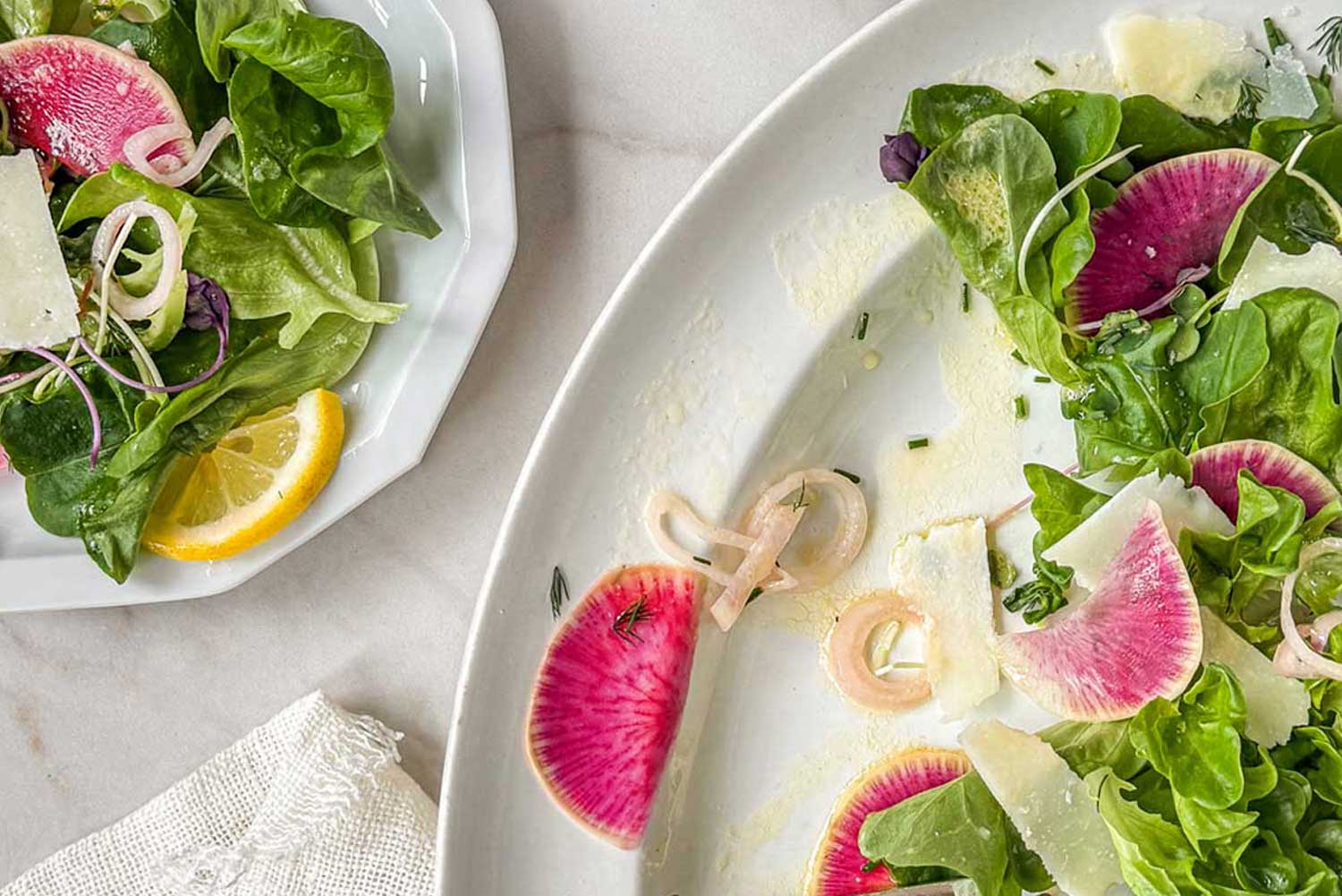 Early spring greens salad with butter lettuce, watermelon radishes, shaved parmesan, and pickled shallots being served on the table at a spring brunch.