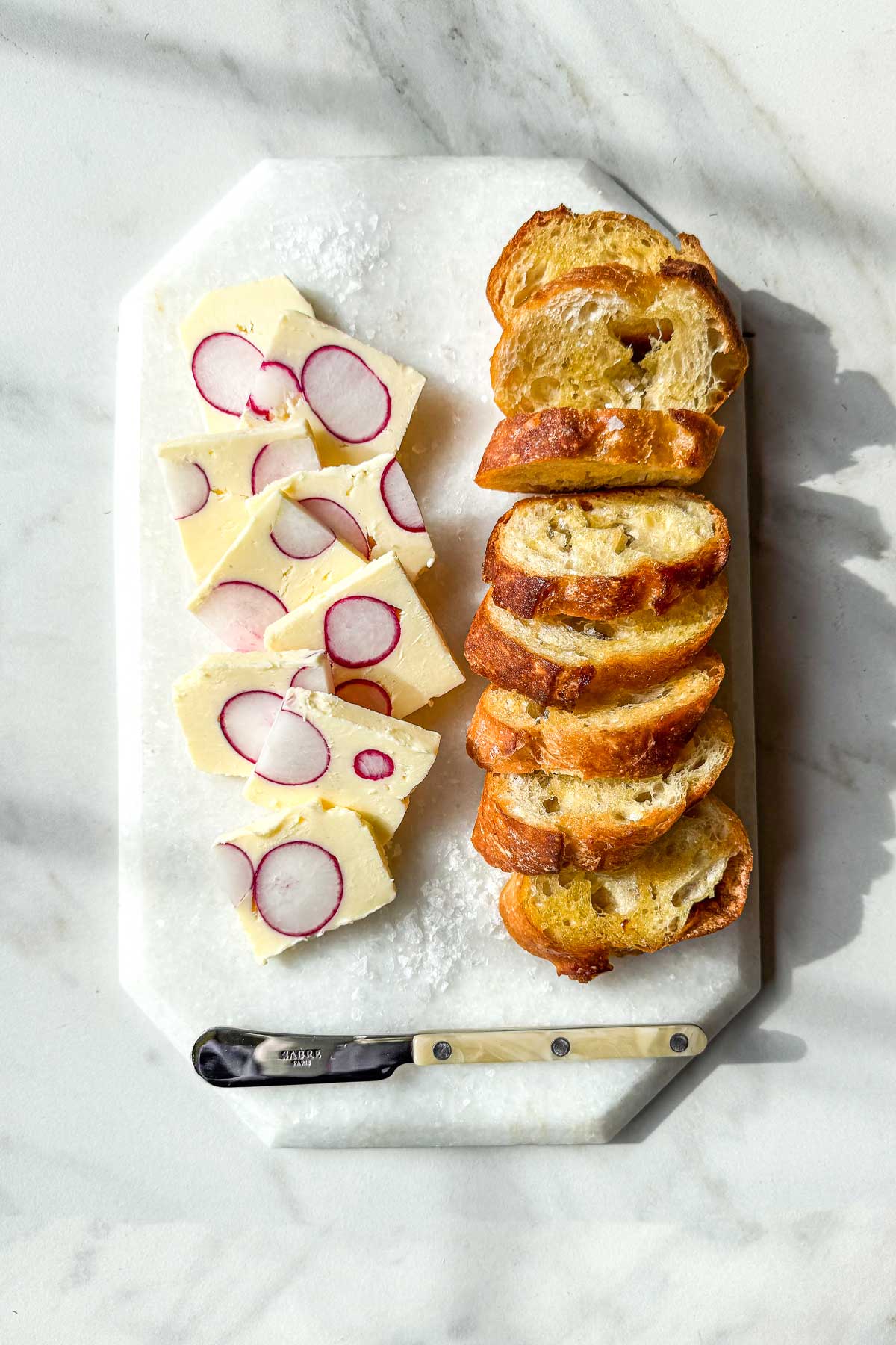 Radish butter terrine slices with whole radish cross-sections served with toasted baguette on a marble board