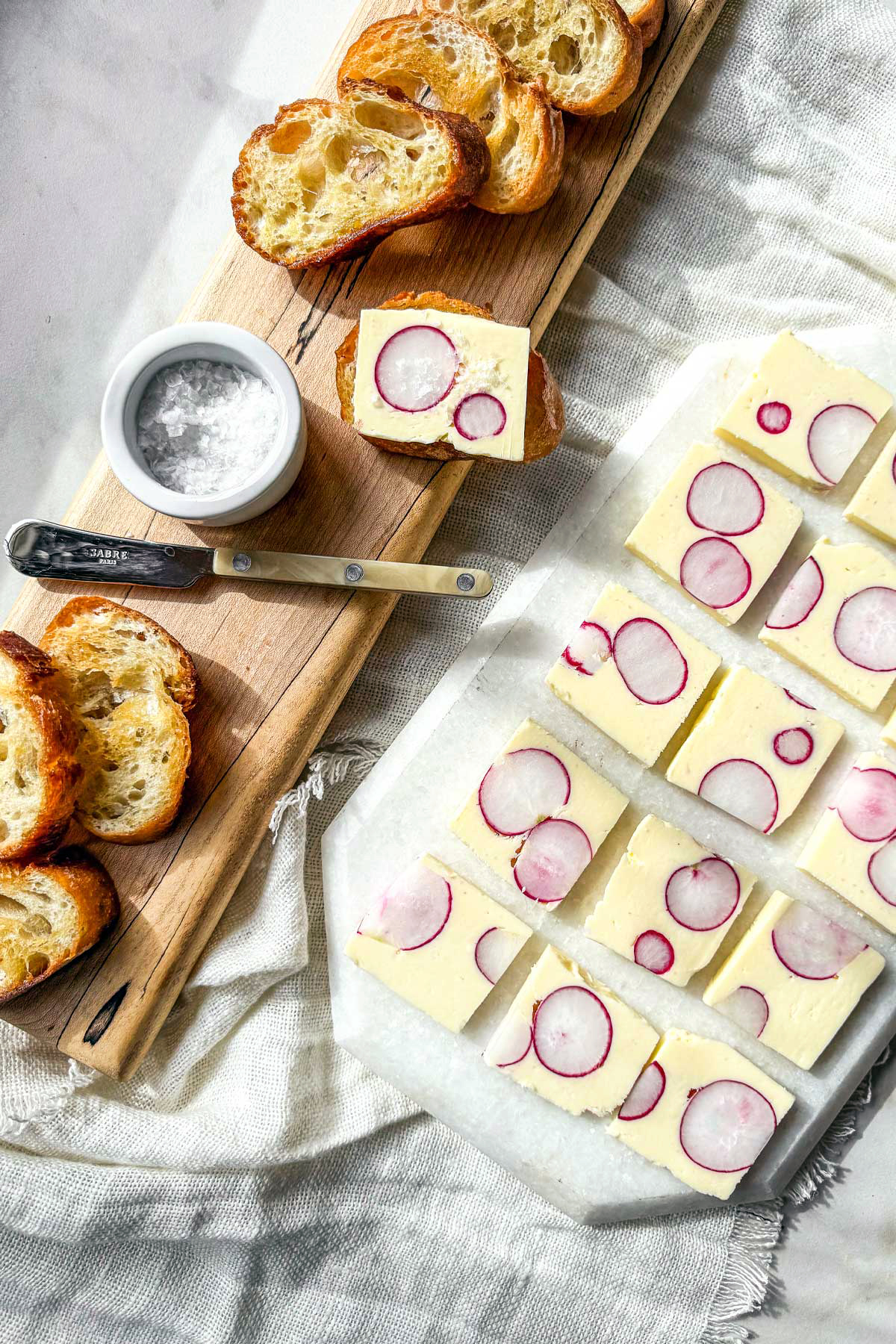 Radish butter terrine slices with whole radish cross-sections served with toasted baguette on a marble board