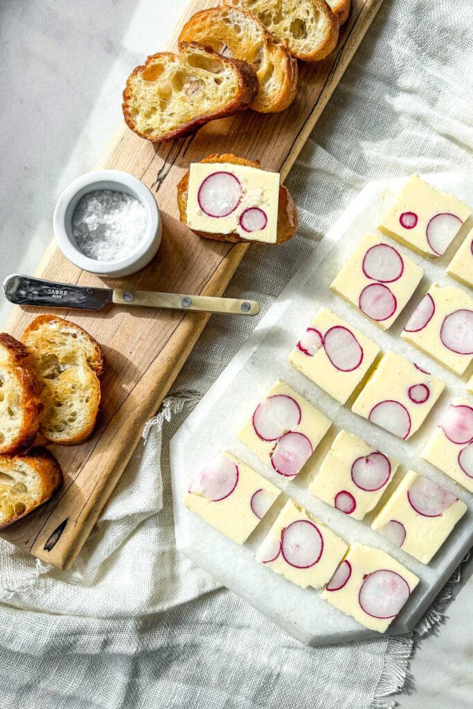 Radish butter terrine slices with whole radish cross-sections served with toasted baguette on a marble board