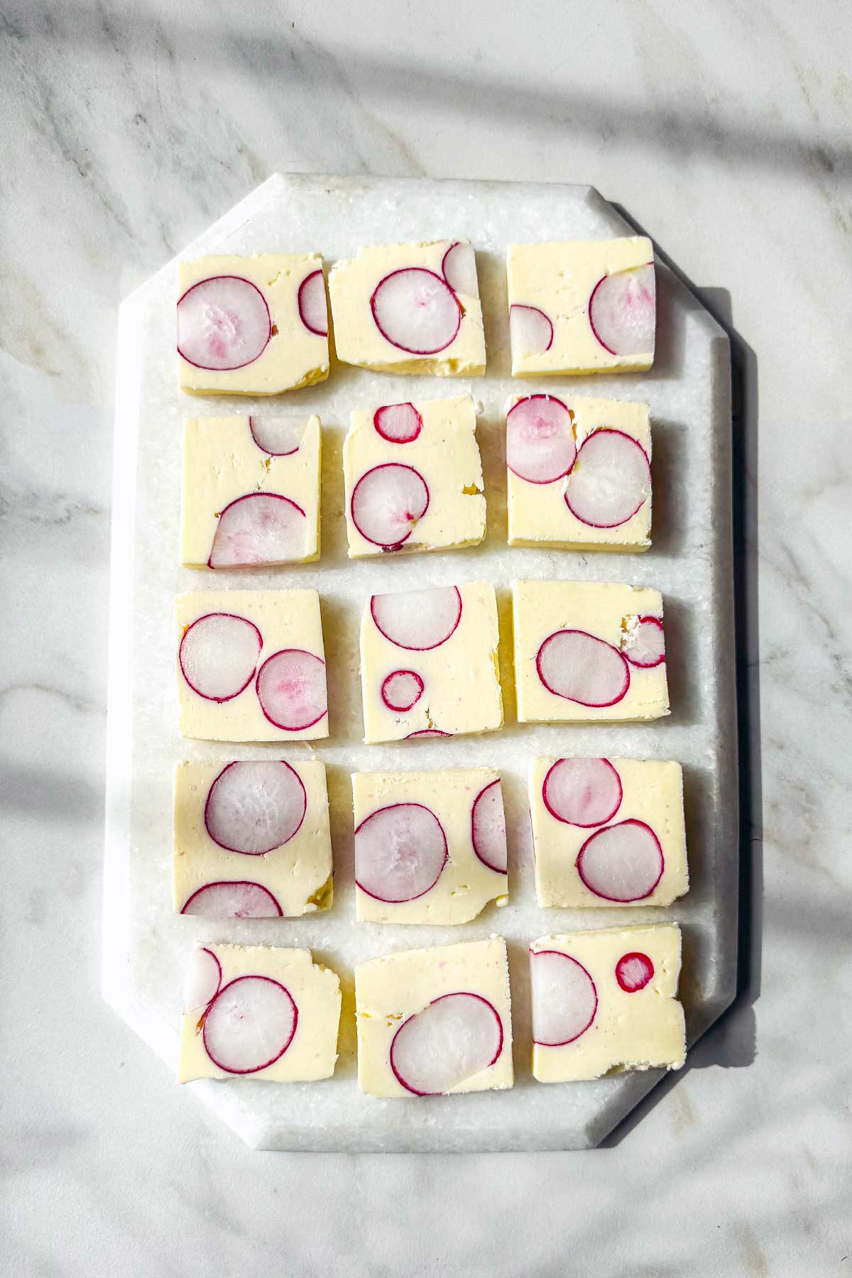 Radish butter terrine slices with whole radish cross-sections served with toasted baguette on a marble board