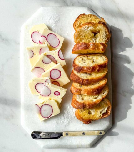 Radish butter terrine slices with whole radish cross-sections served with toasted baguette on a marble board