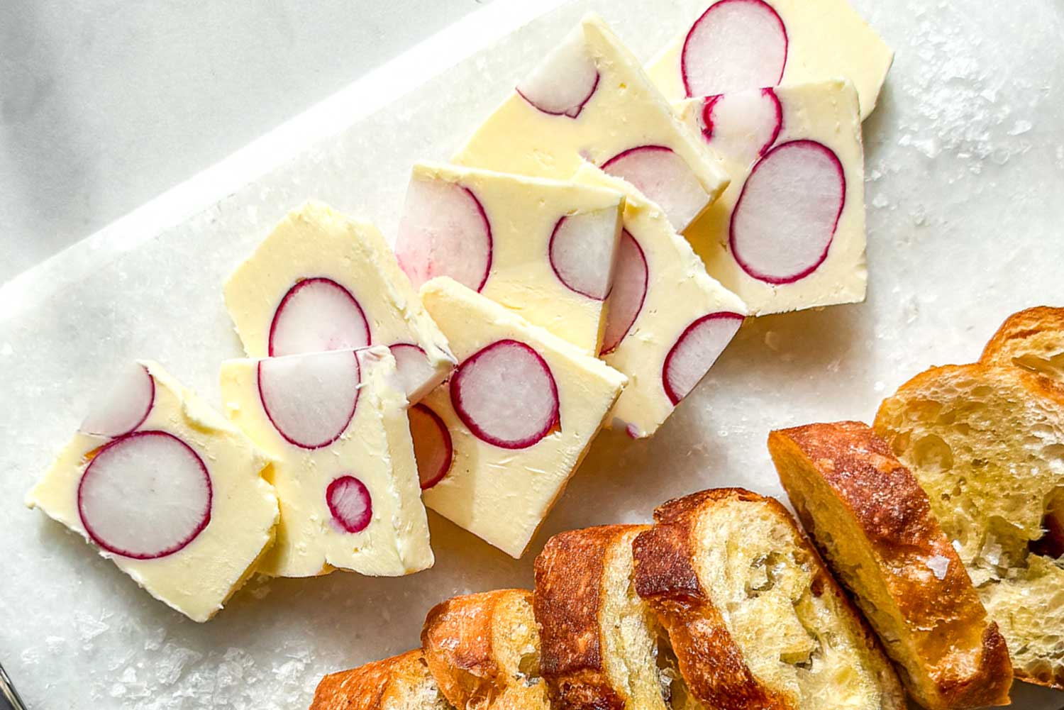 Radish butter terrine slices with whole radish cross-sections served with toasted baguette on a marble board