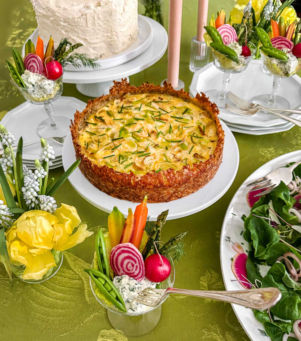 A spring brunch set on the table for Easter or Mother's Day: hashbrown crust quiche, carrot cake, spring greens salad, and crudité