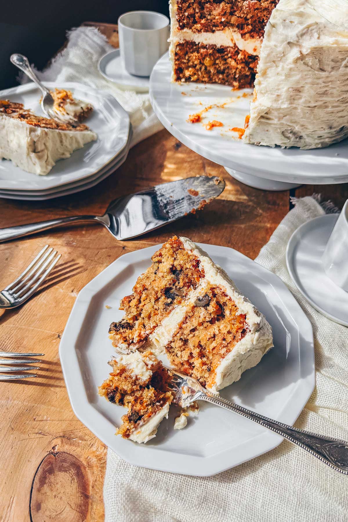 A tiered carrot cake with brown butter cream cheese frosting sliced and served on two plates with coffee.