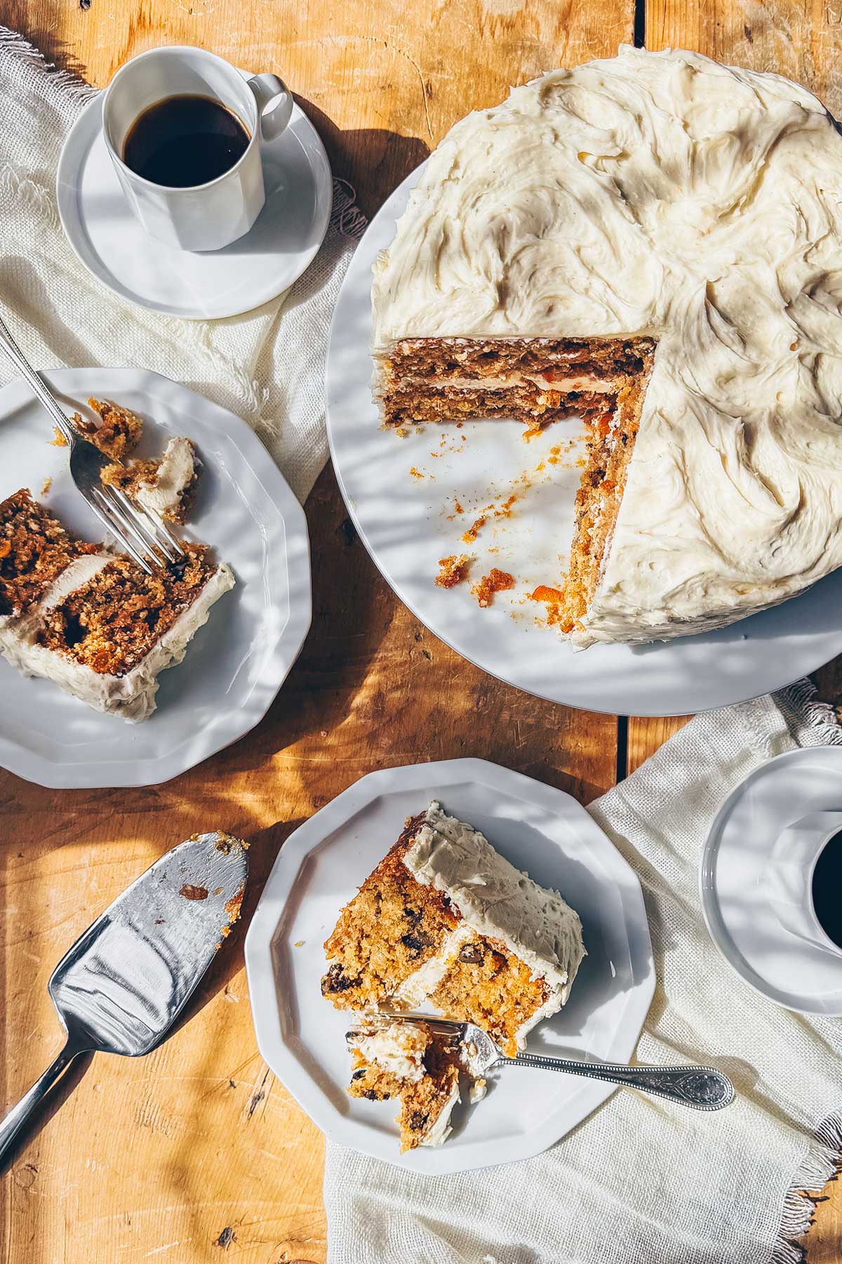 A tiered carrot cake with brown butter cream cheese frosting sliced and served on two plates with coffee.