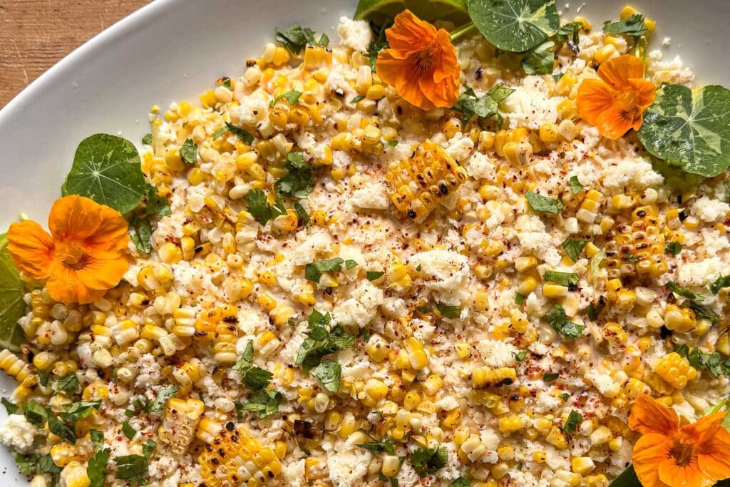Elotรฉ corn dip with grilled corn, Cotija cheese, cilantro, lime, chile, and edible nasturtium flowers